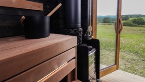 A sauna room with a wooden bench, a black container, and a sauna heater.