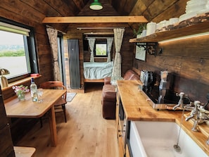 Interior acogedor de una cabaña con una mesa de comedor de madera, una banca, una kitchenette con lavabo y una cama con cortinas.