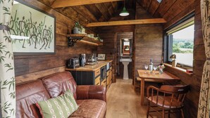 A cabin interior with a wooden ceiling, a kitchenette, a dining area, and a leather sofa.