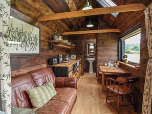 Ein Ferienhäuschen-Interieur mit Holzbalkendecke, einer Küchenzeile, einem Essbereich und einem Ledersofa.