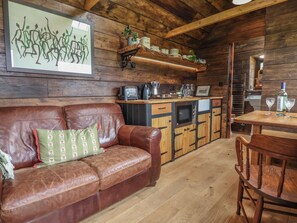 A cozy room with a brown leather sofa, wooden cabinets, and a small dining table with chairs. - Cloud Cabin (Stoke-on-Trent)