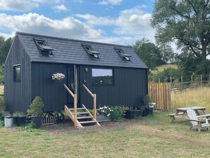 A small, dark wooden cabin with a sloped roof, a front door, and a set of stairs leading up to it. - Cloud Cabin (Stoke-on-Trent)