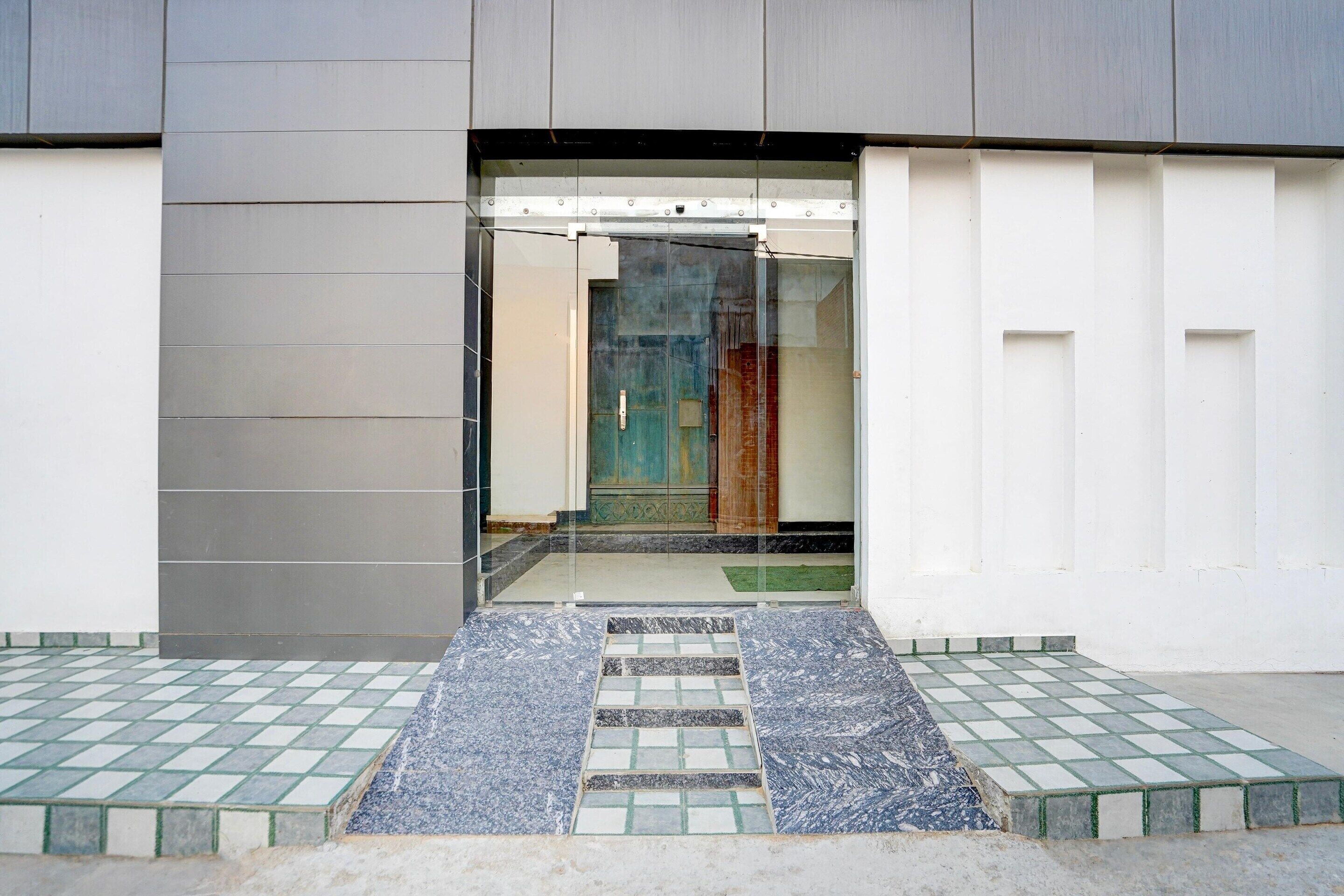 A modern building entrance with a glass door, a tiled floor, and a metal staircase leading inside.