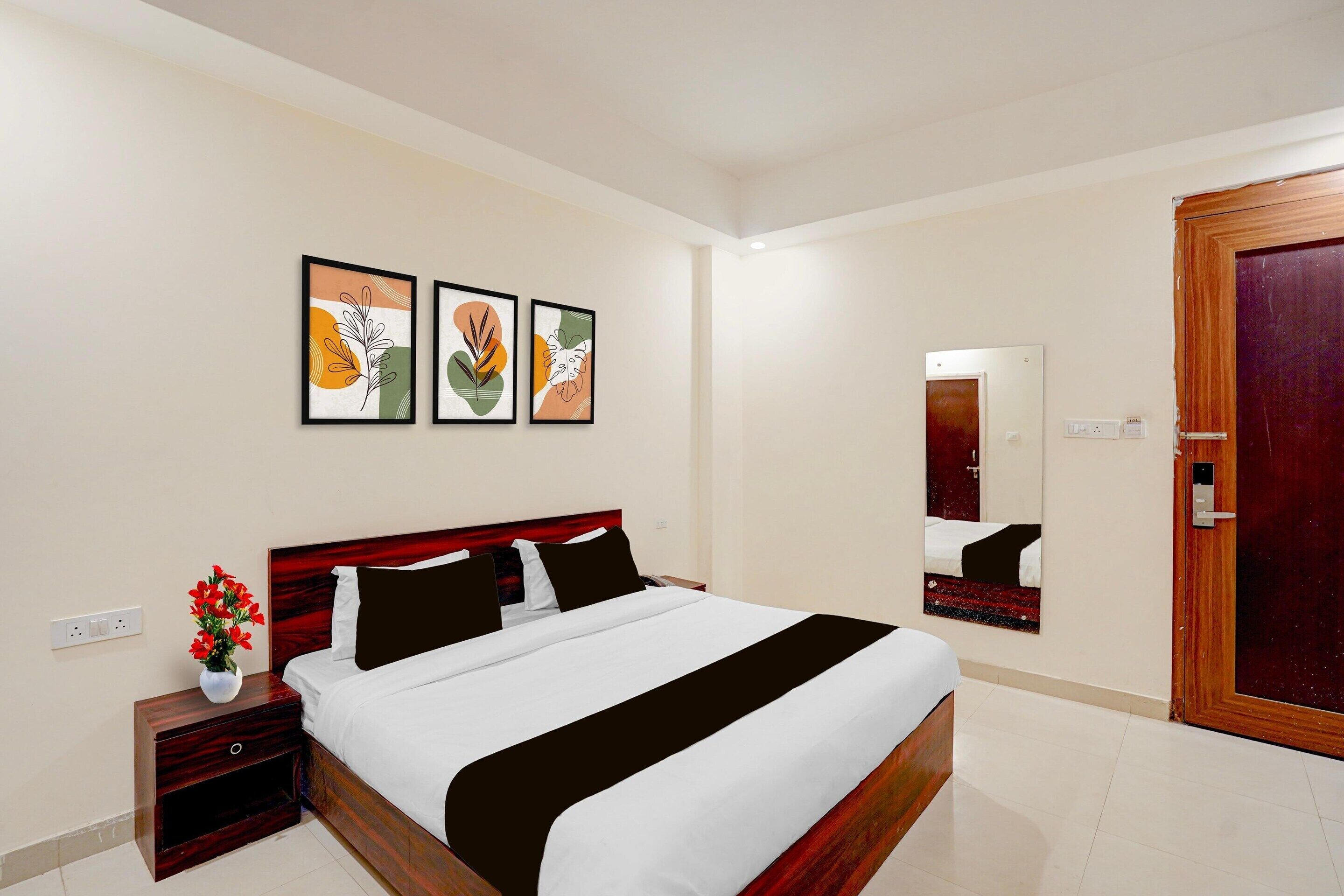 Een hotelkamer met een bed, een nachtkastje, een vaas met bloemen en drie ingelijste kunstwerken aan de muur.