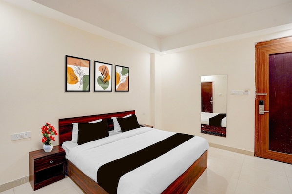 A hotel room with a bed, a nightstand, a vase with flowers, and three framed artworks on the wall.