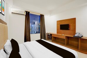 A hotel room with a bed, a desk, a chair, a TV, and a window with curtains. - Suite Room Friends Colony Lucknow (Lucknow)