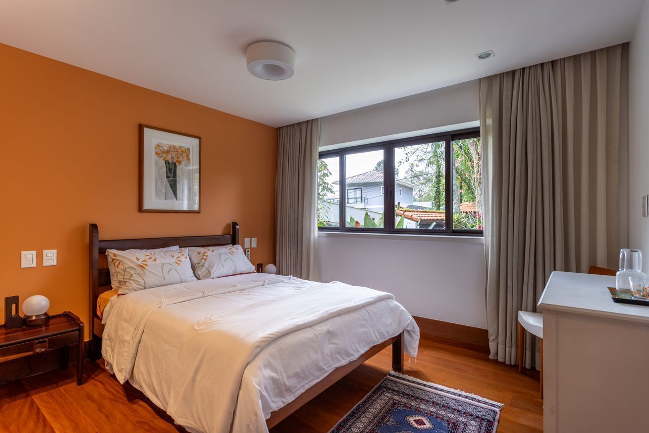 A bedroom with a bed, a bedside table, a window with curtains, and a view of the outside.