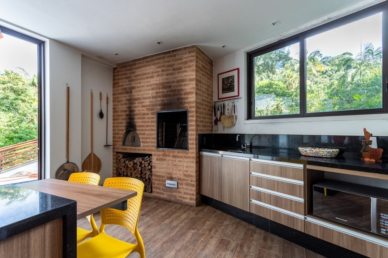 A modern kitchen with a brick wall, wooden cabinets, a black countertop, and a large window with a view of greenery.