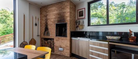 A modern kitchen with a brick wall, wooden cabinets, a black countertop, and a large window with a view of greenery.