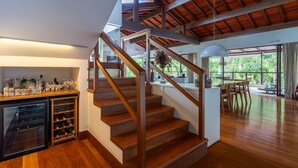 A spacious interior with a wooden staircase, a kitchen area, and a dining space with a view. - Casa com Lareira e Piscina Perto da Granja Comary (Teresópolis)