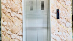 Un ascensor moderno con un revestimiento de pared con diseño de mármol, techo con líneas verticales y una pantalla digital en la pared.