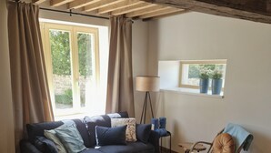 Ein Wohnzimmer mit einer Couch, einem Sessel, einer Lampe und einem Fenster mit Pflanzen.