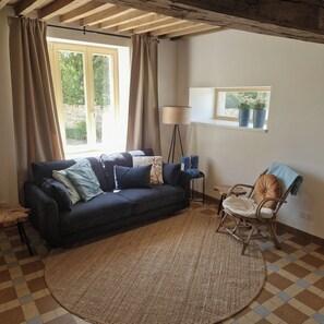 Ein Wohnzimmer mit einer Couch, einem Sessel, einer Lampe und einem Fenster mit Pflanzen.