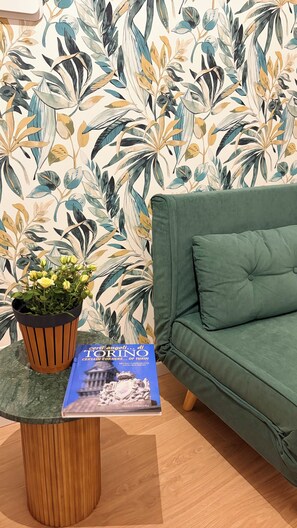 Ein grünes Sofa, ein Blumentopf und ein Buch mit dem Titel 'Certi angoli di Torino' auf einem Holztisch.