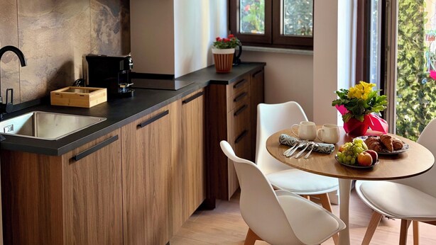 Una cocina moderna con armarios de madera, encimera negra y una zona de comedor con sillas y mesa blancos.