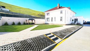 Une maison blanche avec un toit rouge, une allée pavée et un véhicule noir garé dans l’allée.