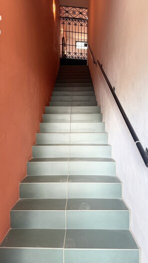 A staircase with alternating light and dark tiles, a metal railing on one side, and a decorative metal gate at the top. - Suite Federalismo Center (Guadalajara)