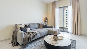 Ett modernt vardagsrum med en grå soffa, ett runt soffbord och ett stort fönster med gardiner.