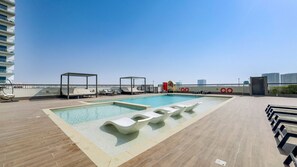 Un área de piscina en la azotea con sillones de descanso, una piscina pequeña y vistas del horizonte de la ciudad.