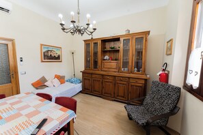A room with a dining table, a sofa, a patterned armchair, a wooden cabinet, a chandelier, and a painting on the wall. - Lucia's Charming Apartment (Firenze)