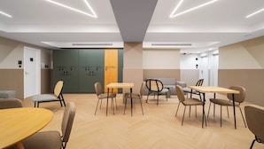 Ein moderner Konferenzraum mit Fischgrätparkett, Holztischen und -stühlen, einer Wand mit Fischgratmuster und einer Tür mit nummerierten Schließfächern.