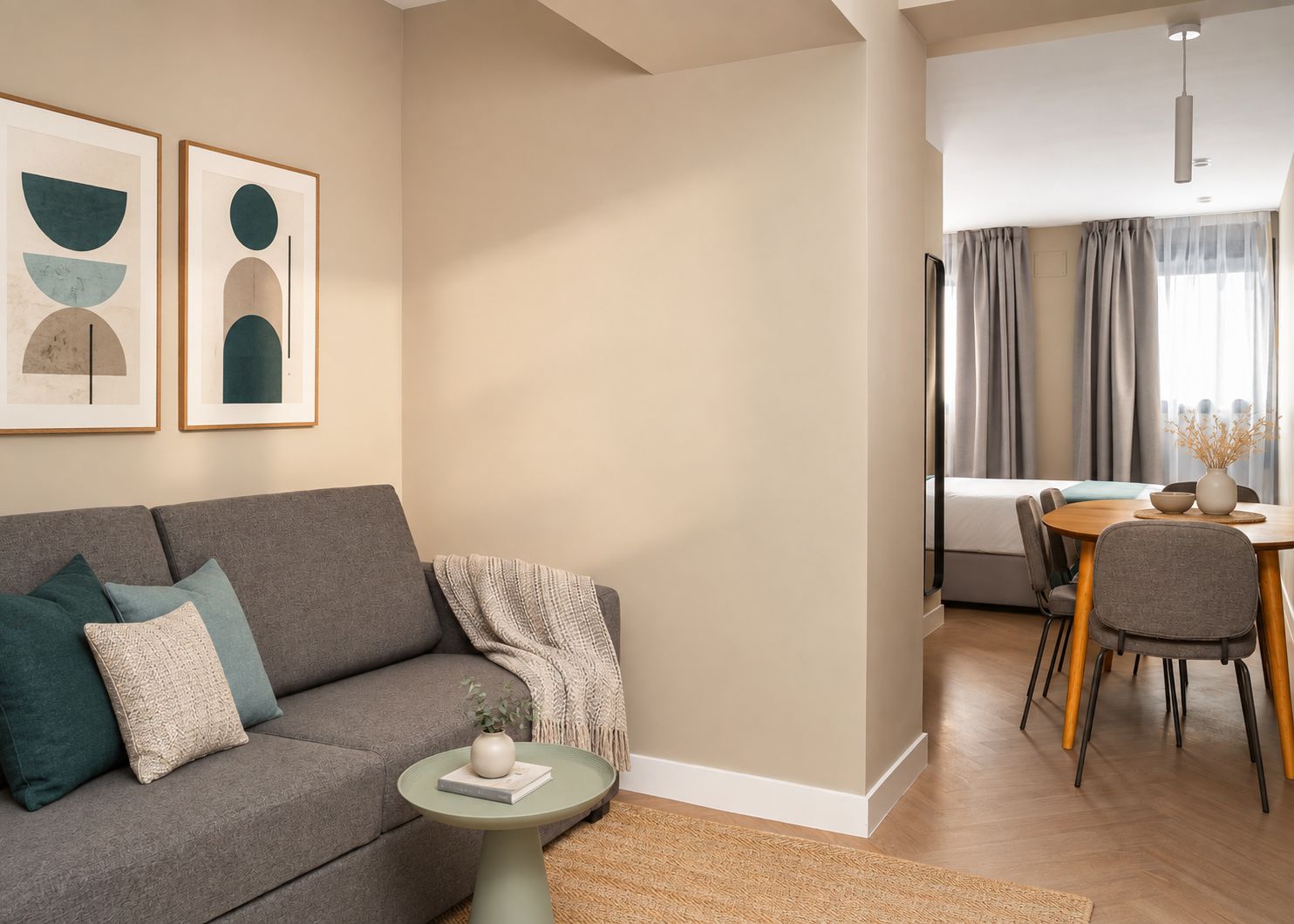 A modern living room with a grey sofa, a small round table, and a dining area with a wooden table and chairs.