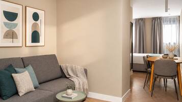 A modern living room with a grey sofa, a small round table, and a dining area with a wooden table and chairs.