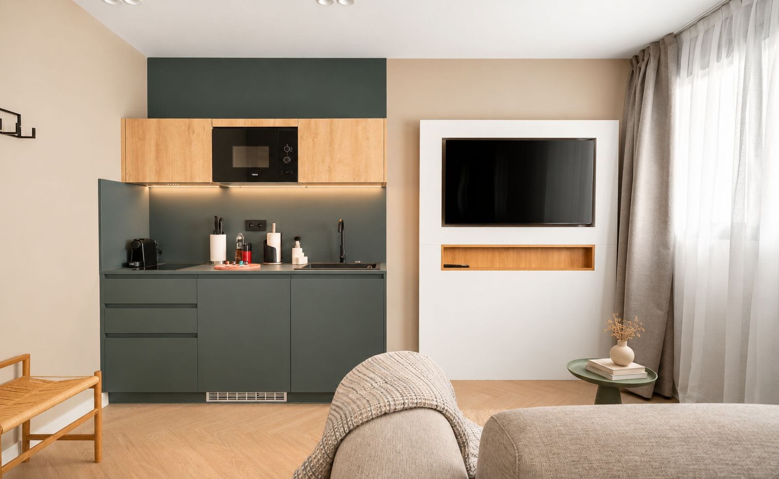 Cocina moderna con microondas, lavaplatos y armarios de madera. Hay un televisor de pantalla plana en la pared y una pequeña mesa con un florero y libros.