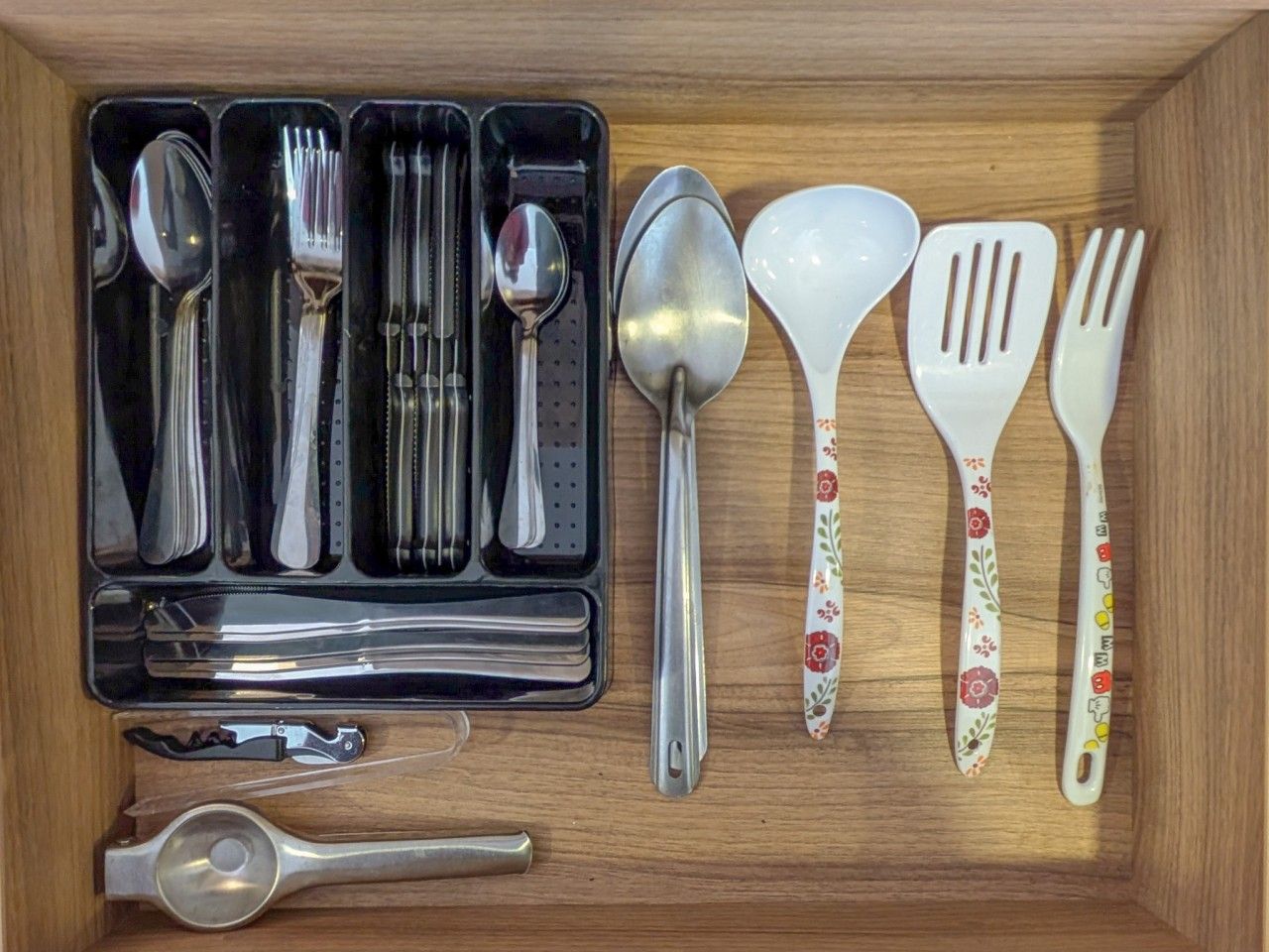 A wooden drawer containing a set of utensils including spoons, forks, and a spatula.