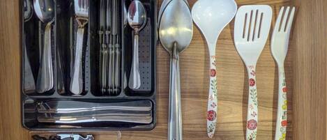 A wooden drawer containing a set of utensils including spoons, forks, and a spatula.