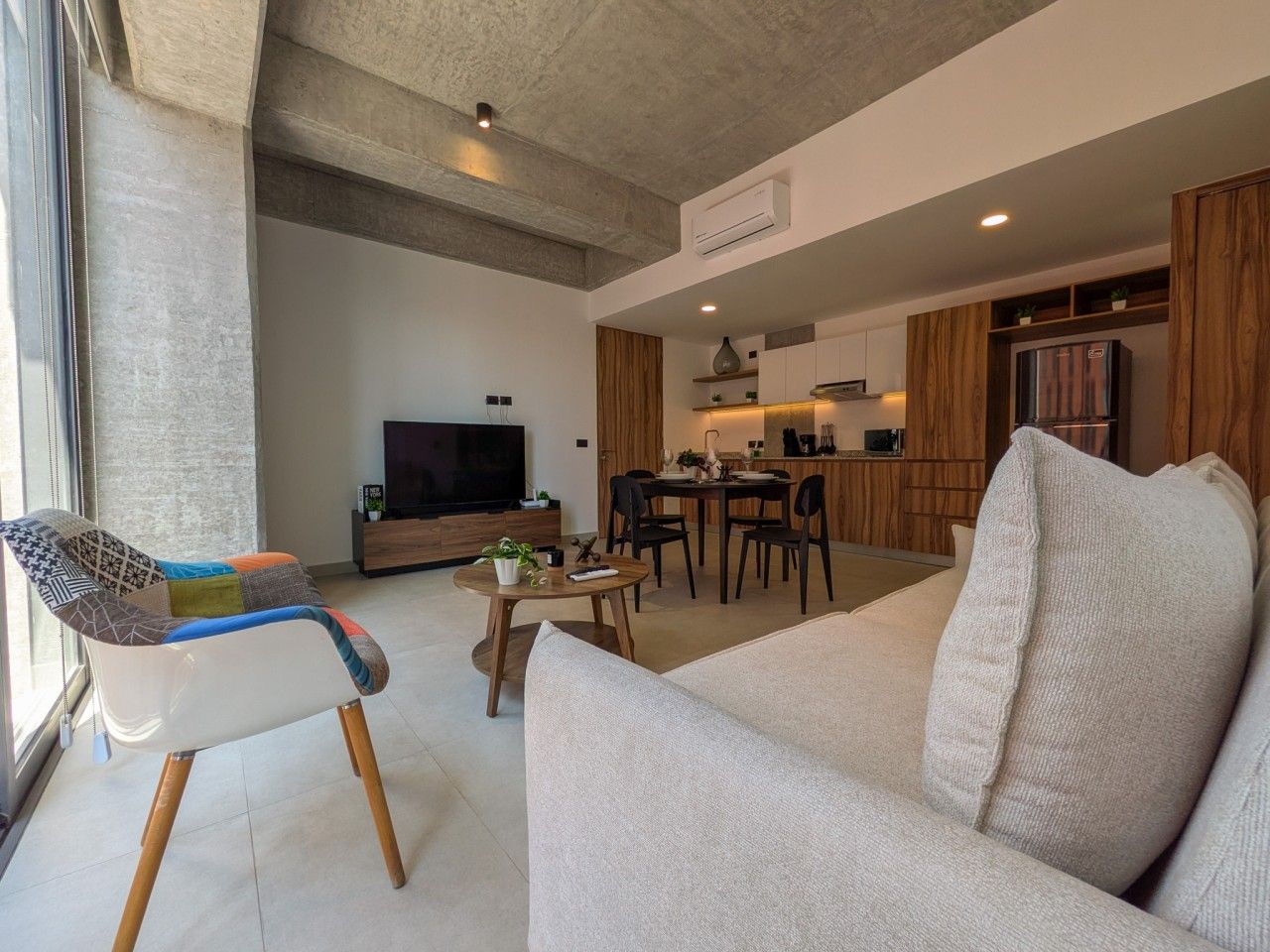 Een moderne woonkamer met een bank, een kleurrijke fauteuil, een eethoek en een keuken op de achtergrond.