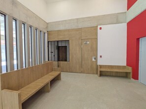 Een wachtruimte met houten banken, een rode muur en een deur.