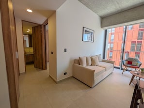 A living room with a sofa, a dining table, and a chair. There is a window with a view of buildings. - Moderno Loft en Av. México | Ubicación Premium (Guadalajara)