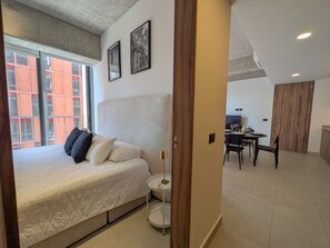 Ein Schlafzimmer mit Bett, Nachttisch und Blick auf die Stadt durch große Fenster.