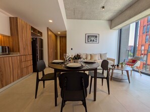 A modern kitchen with built-in appliances, a dining area with a round table and chairs, and a large window offering a view of the city. - Moderno Loft en Av. México | Ubicación Premium (Guadalajara)