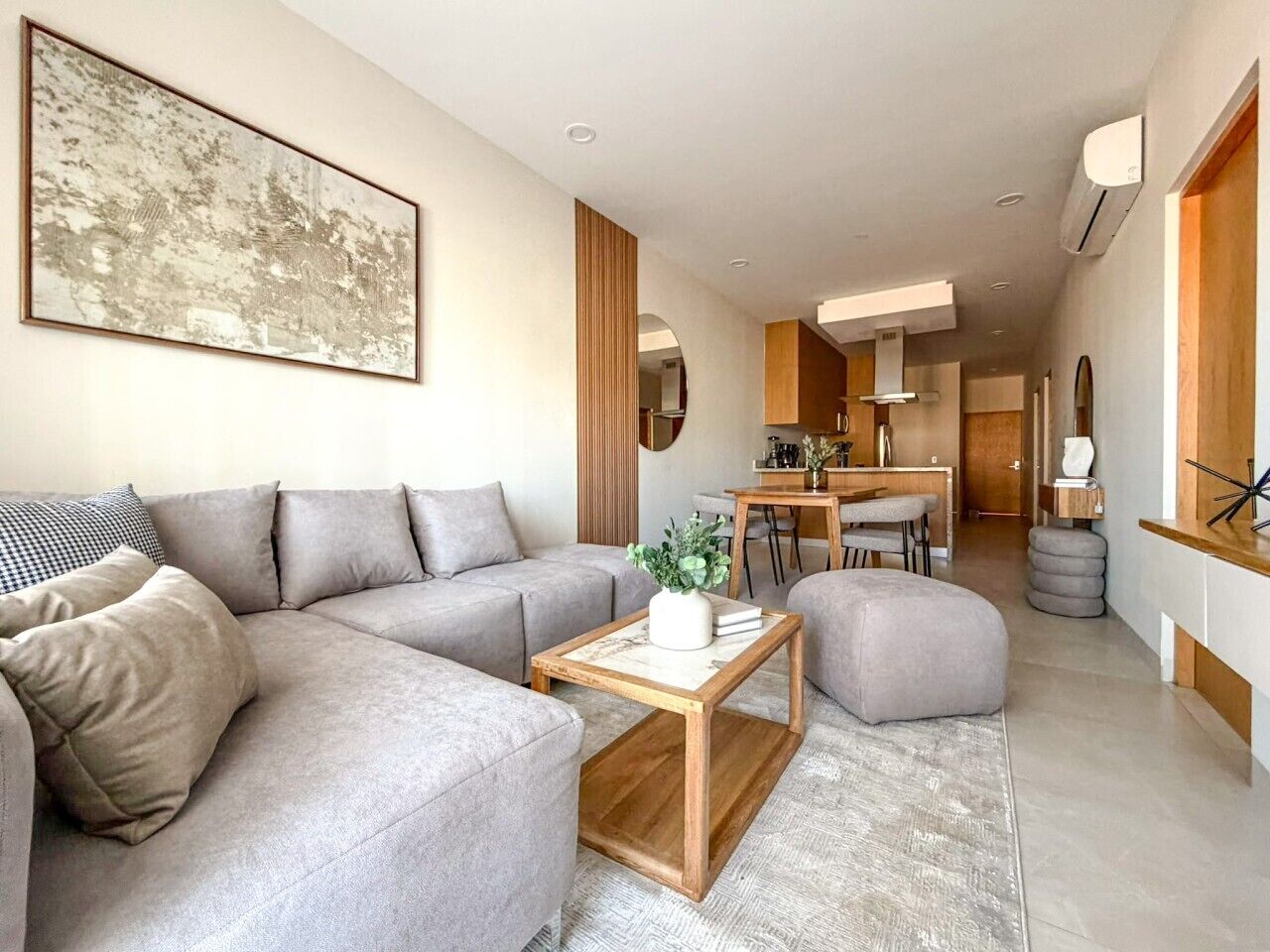 A modern living room with a sectional sofa, a coffee table, and a dining area with a kitchen in the background.