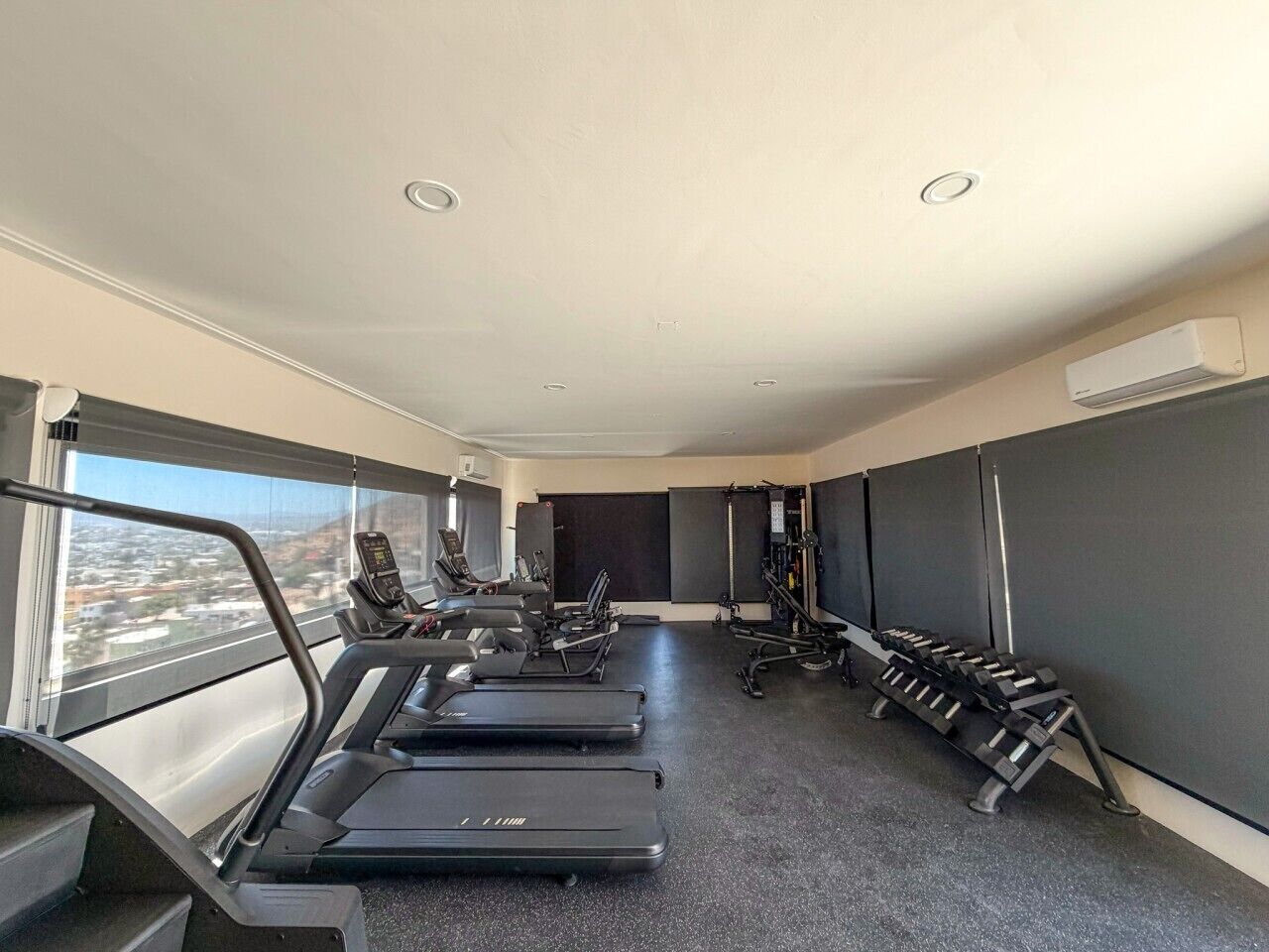 A gym with treadmills, weight machines, and a large window with a city view.