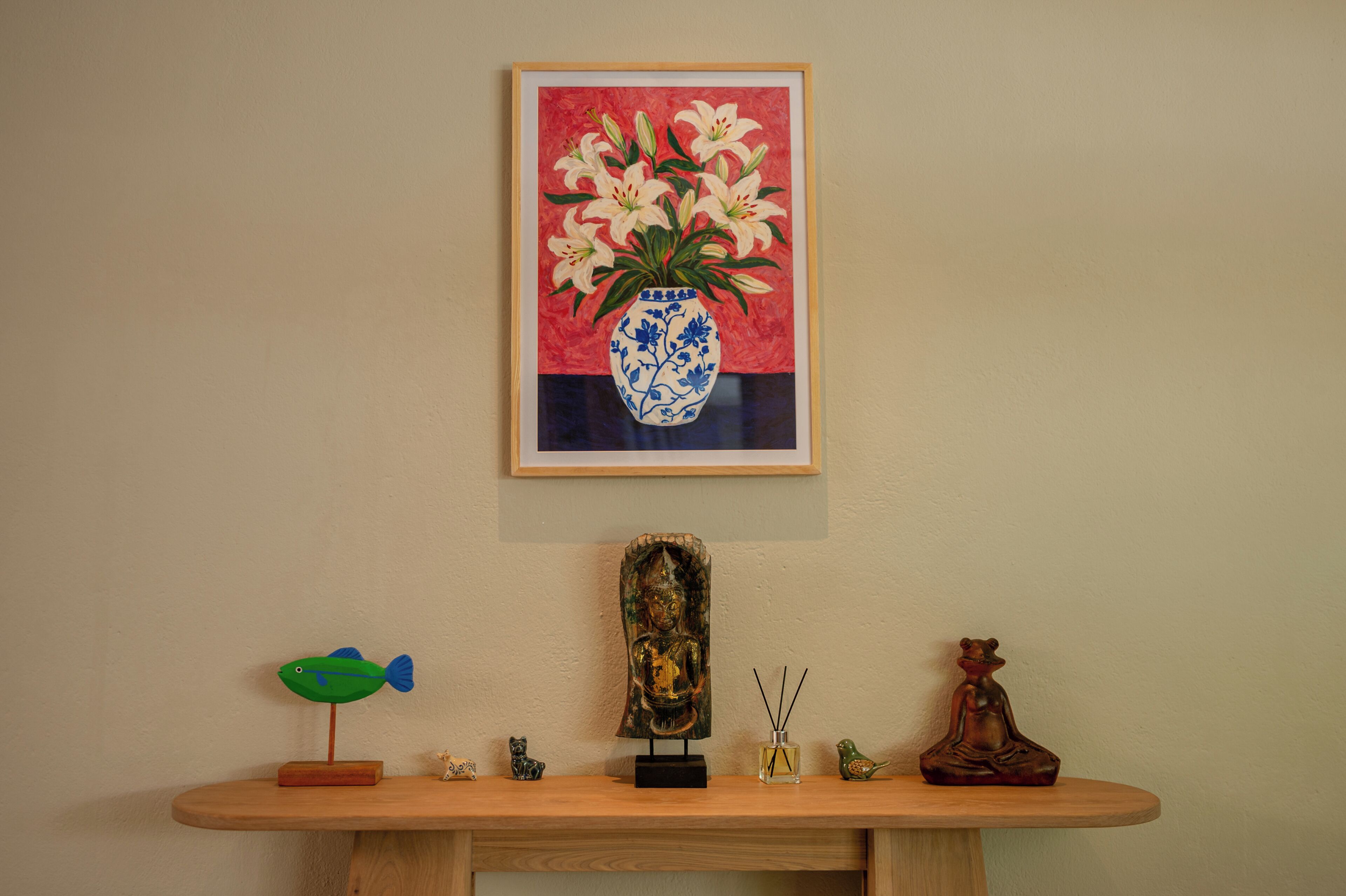 Ett konsolbord i trä med en inramad tavla, en Buddha-staty, en liten Buddha-figur, en lampa formad som en fisk och en liten Buddha-staty.