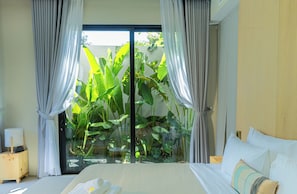 Ein Schlafzimmer mit Bett, Vorhängen, einem Nachttisch und Blick auf Grün hinter einer Glastür.
