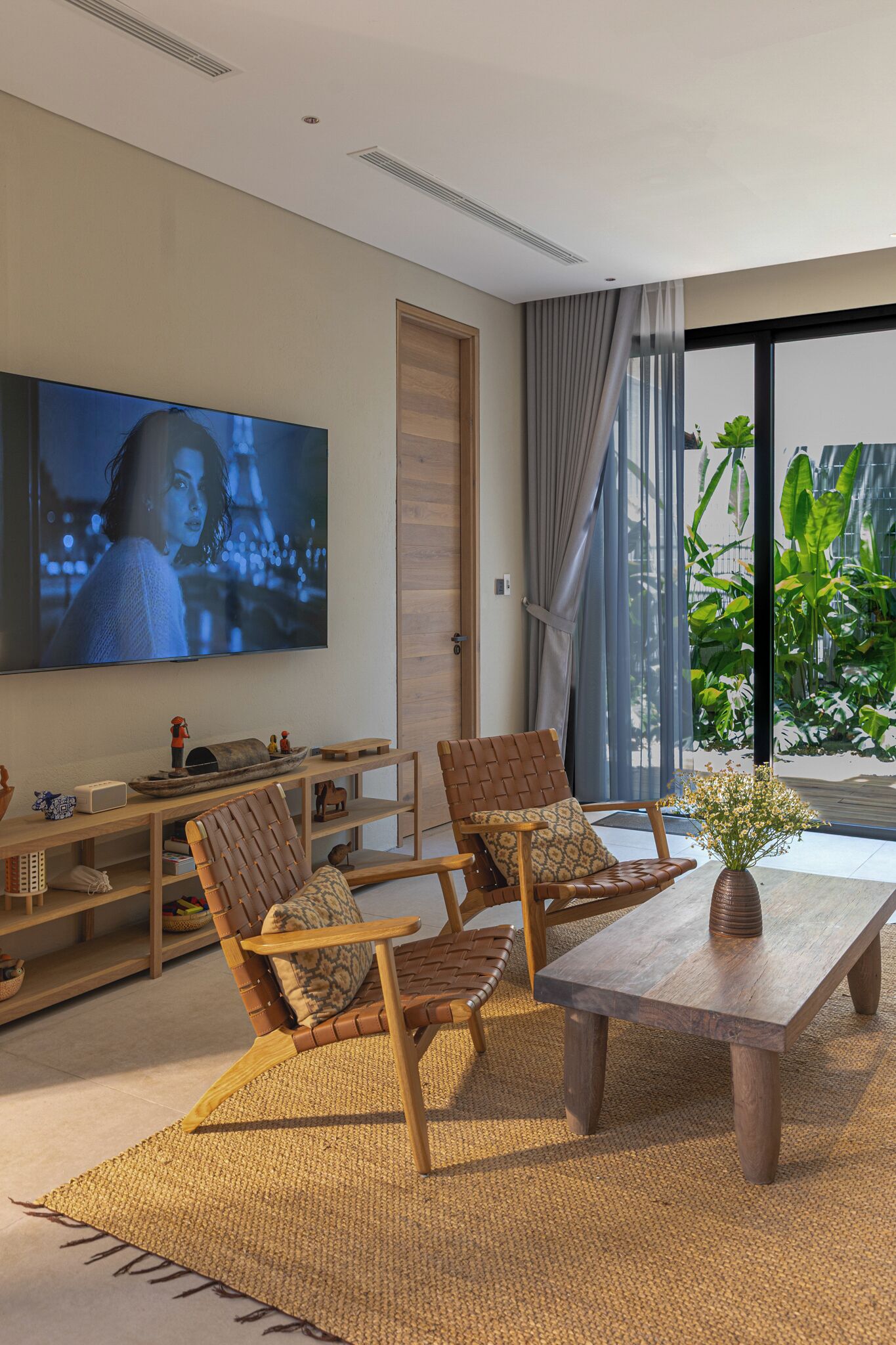 Una sala de estar moderna con un televisor de pantalla plana, dos sillones de cuero, una mesa de centro de madera y un gran ventanal con cortinas.