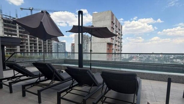 En takterrass med solstolar och parasoller, med utsikt över en stadssiluett med byggnader och en klar himmel.
