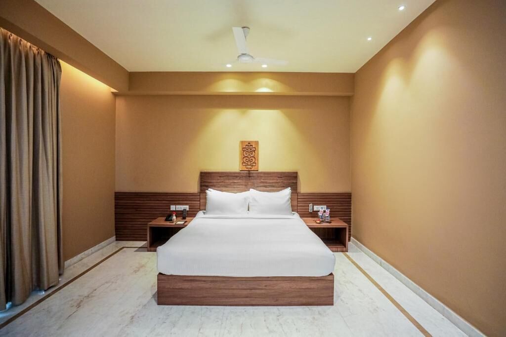 Una habitación de hotel con una cama grande, cabecera de madera, mesitas de noche y un ventilador de techo.