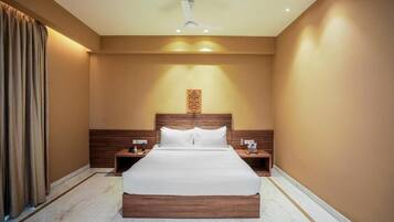 Una habitación de hotel con una cama grande, cabecera de madera, mesitas de noche y un ventilador de techo.