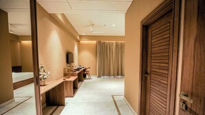 A hotel corridor with a wooden door, a desk with a computer, and a large window with curtains. - Gulab Kothi by Grapevine Varanasi (Varanasi)