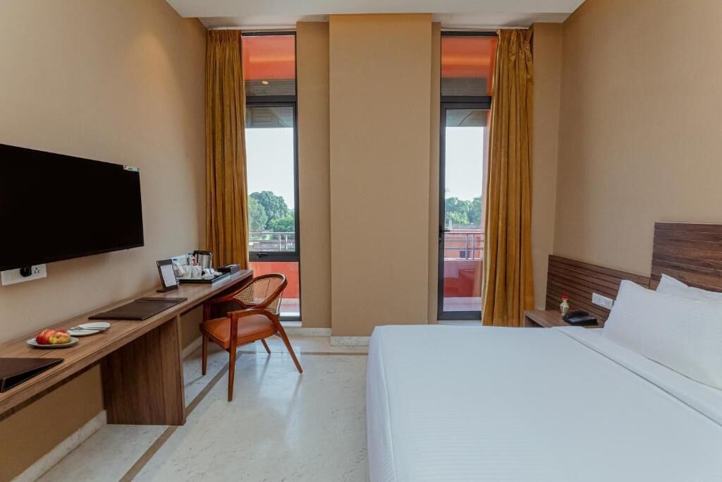 A hotel room with a bed, a desk, a chair, a television, and a window with curtains.