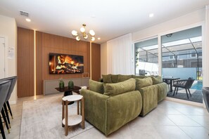 A modern living room with a green sofa, a flat-screen TV, and a fireplace. - Modern 5 Bedroom Townhome at Windsor Cay 89BL (Clermont)