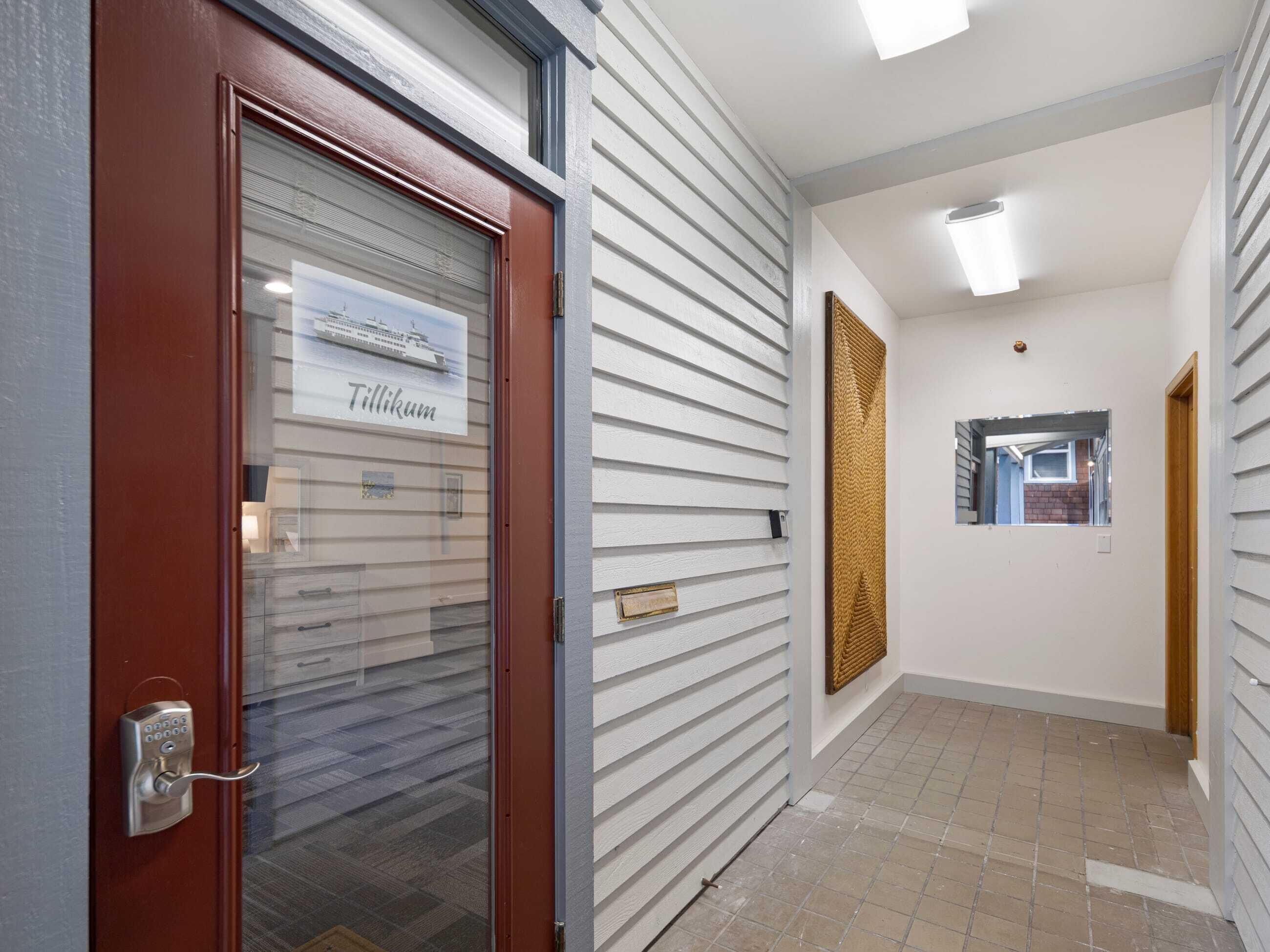 Un couloir avec une porte rouge, une enseigne indiquant « Tillikum » et un mur à texture.