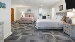 Een hotelkamer met twee bedden, een kitchenette, een televisie en een schilderij aan de muur.