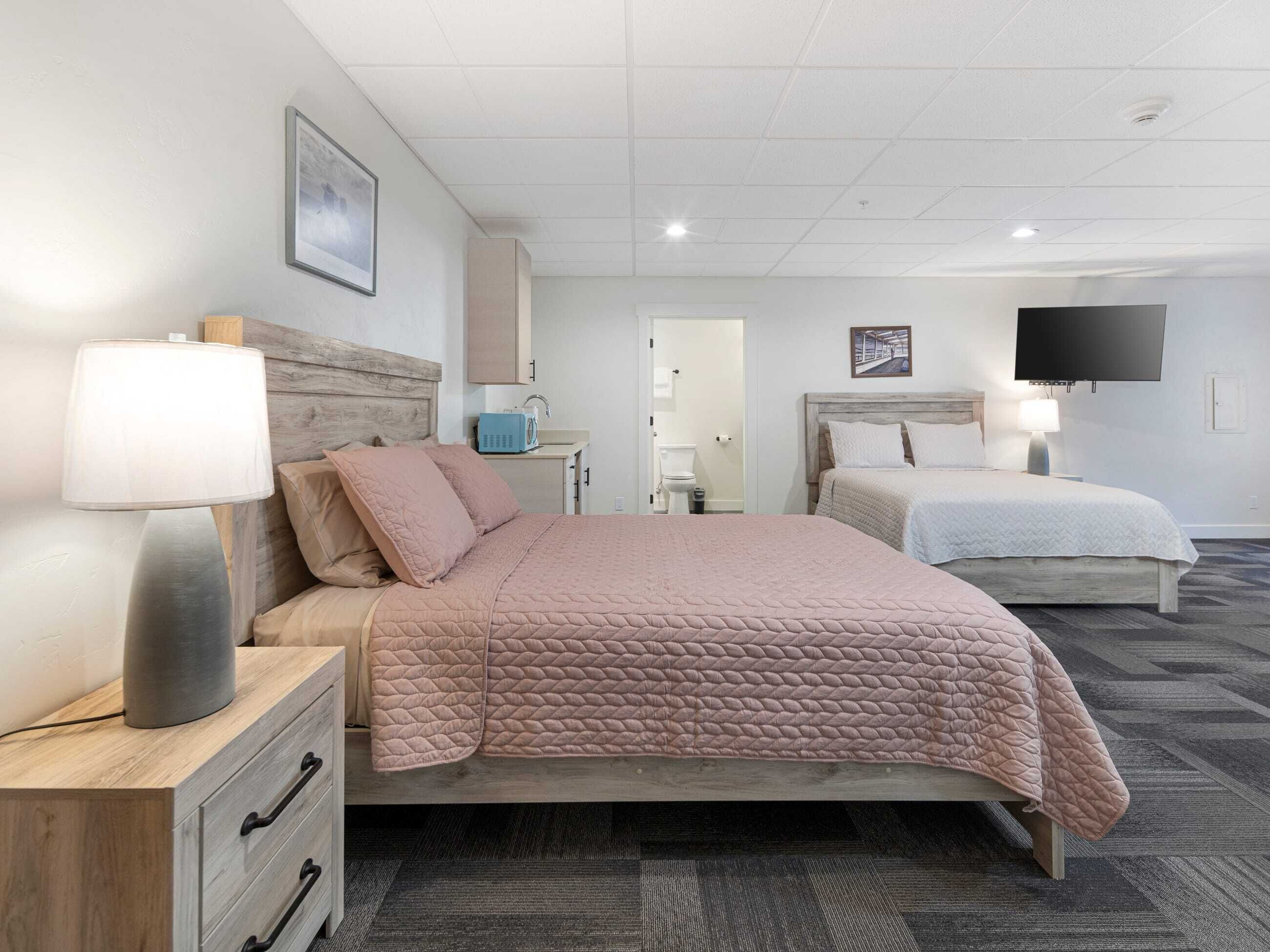 A hotel room with a bed, bedside table, lamp, and a television on the wall.