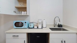 Een kleine keuken met een magnetron, broodrooster, koffiezetapparaat en spoelbak.